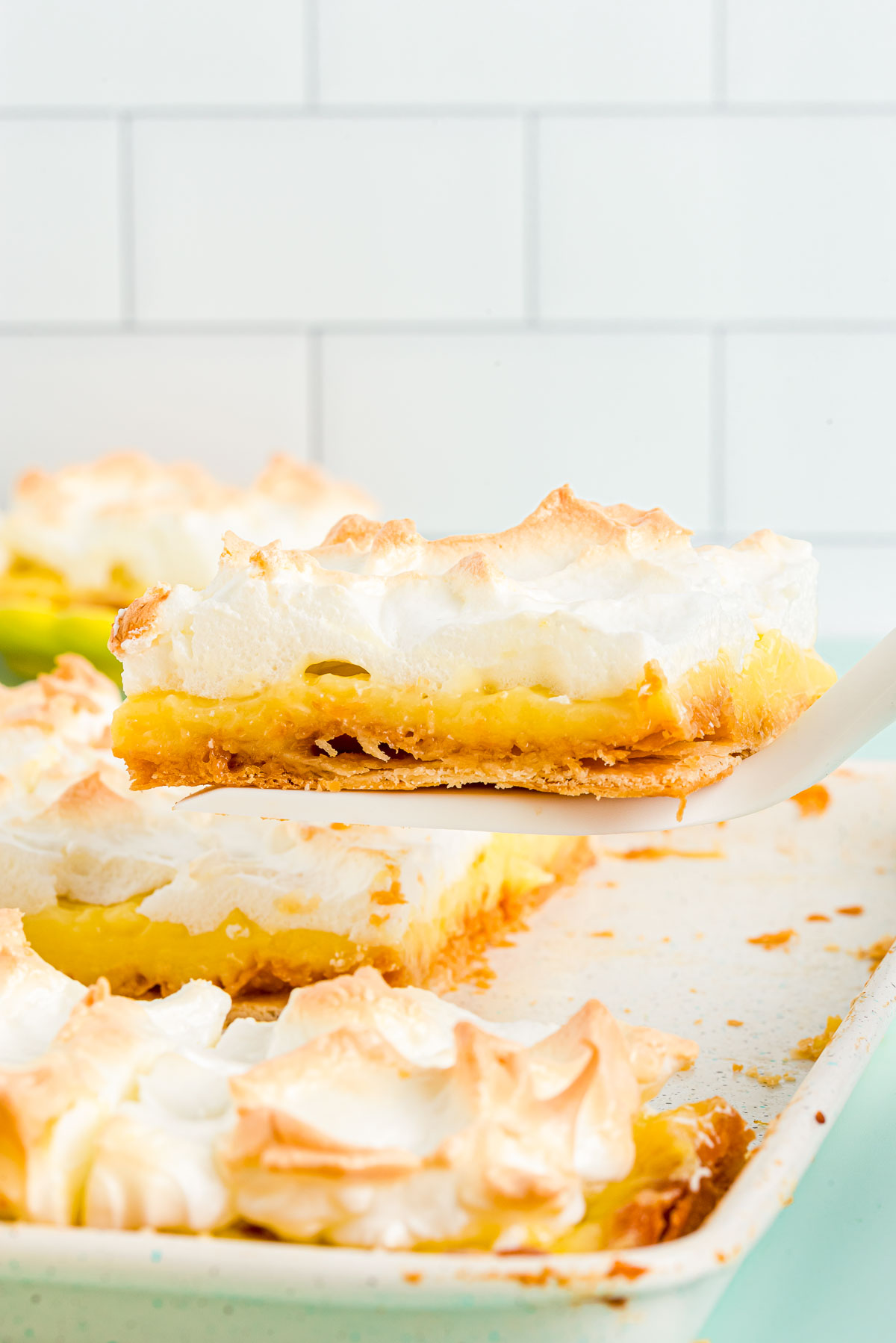 A slice of lemon meringue slab pie being lifted from the pan.