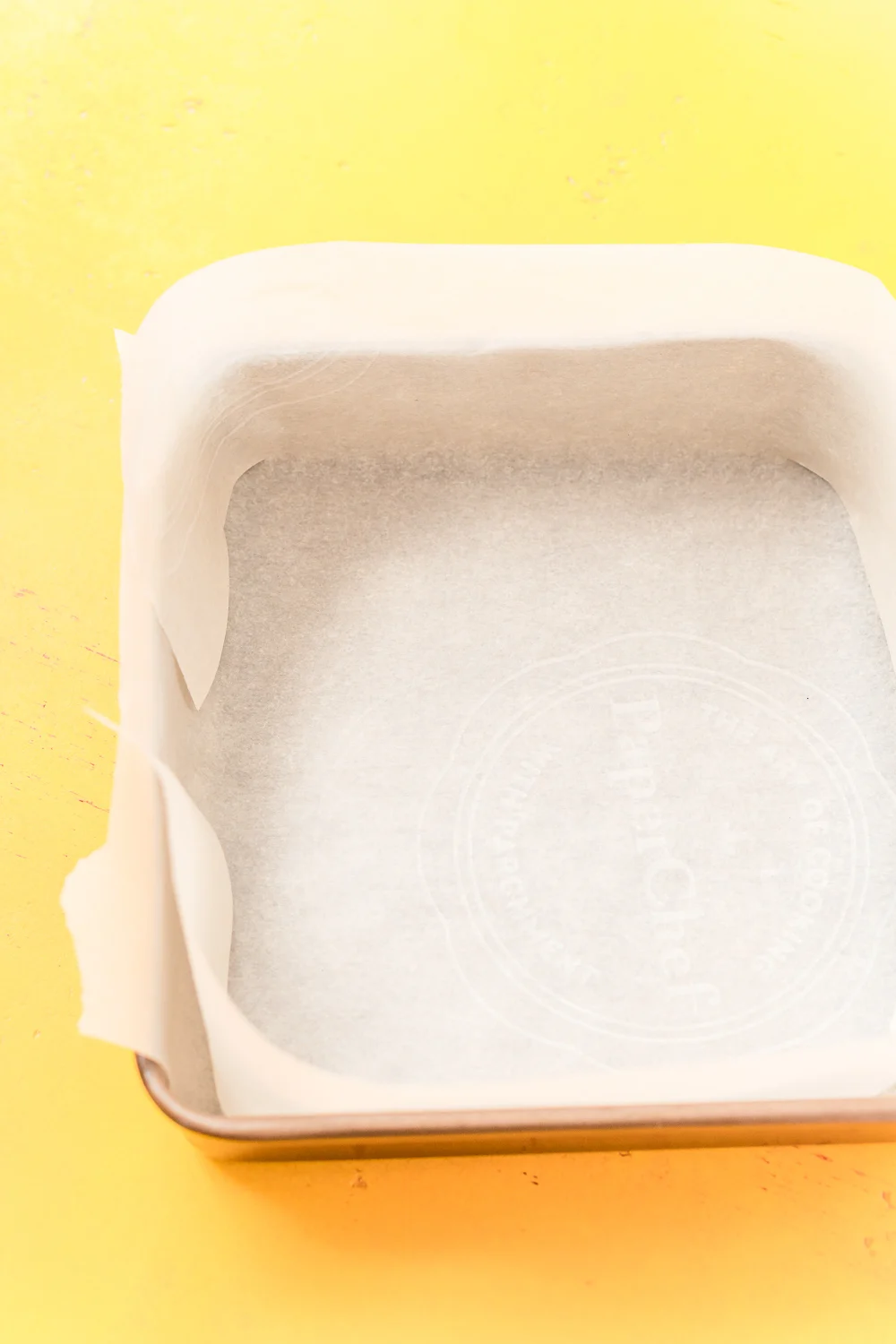 Parchment paper lining a baking pan on yellow surface.