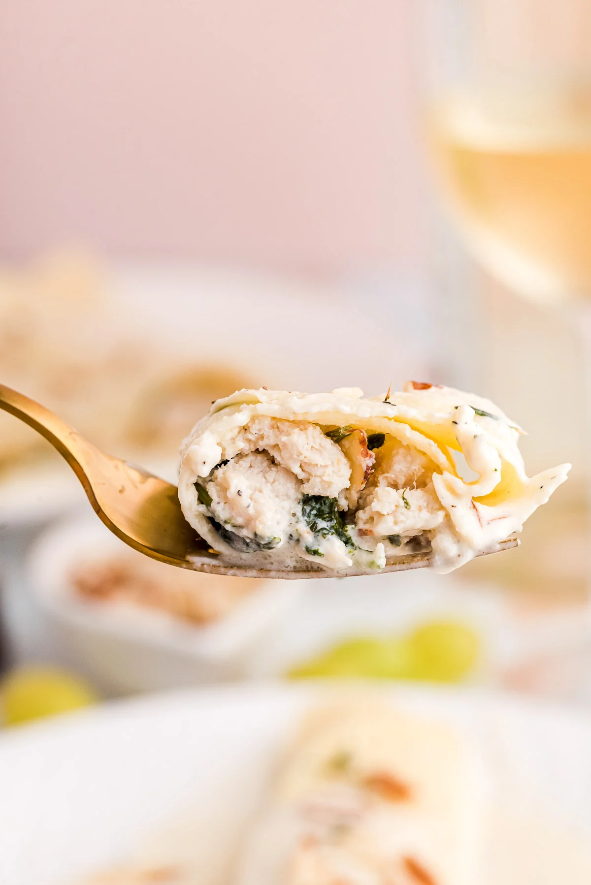 A bite of spinach and chicken crepe on a gold fork being held close to the camera.