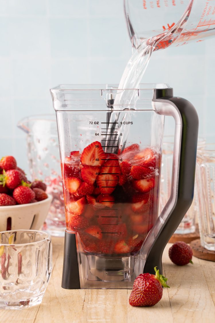 Water being added to a blender with strawberries, lemon juice, and simple syrup.