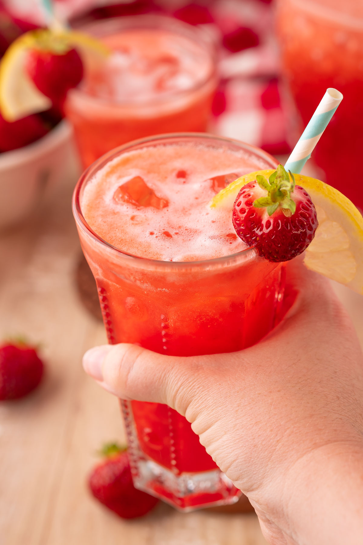 A woman's hand holding a glass of strawberry lemonade to the camera.