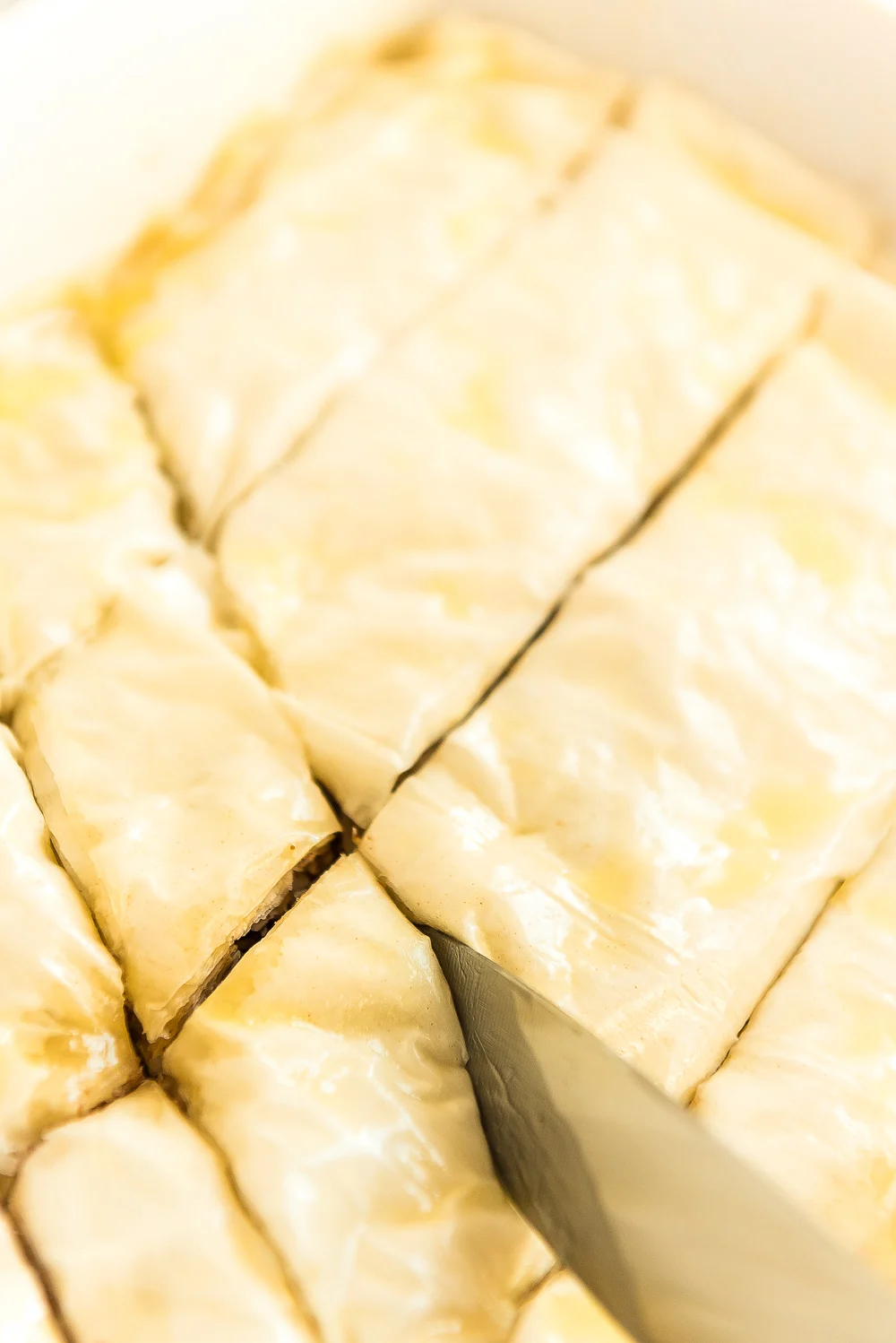 Baklava being cut with a large knife before going in the oven.