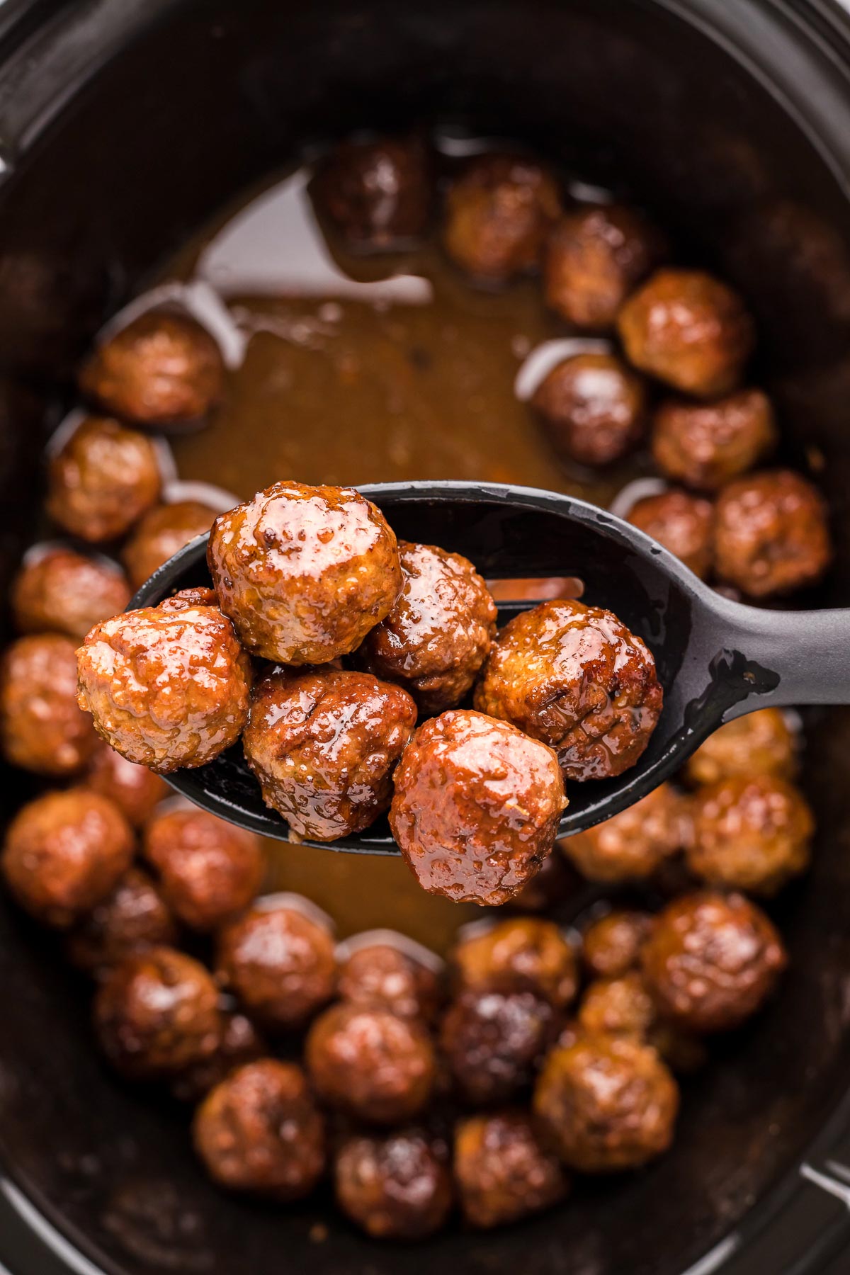 Close up photo of a serving spoon scooping merlot meatballs out of a crockpot and towards the camera.