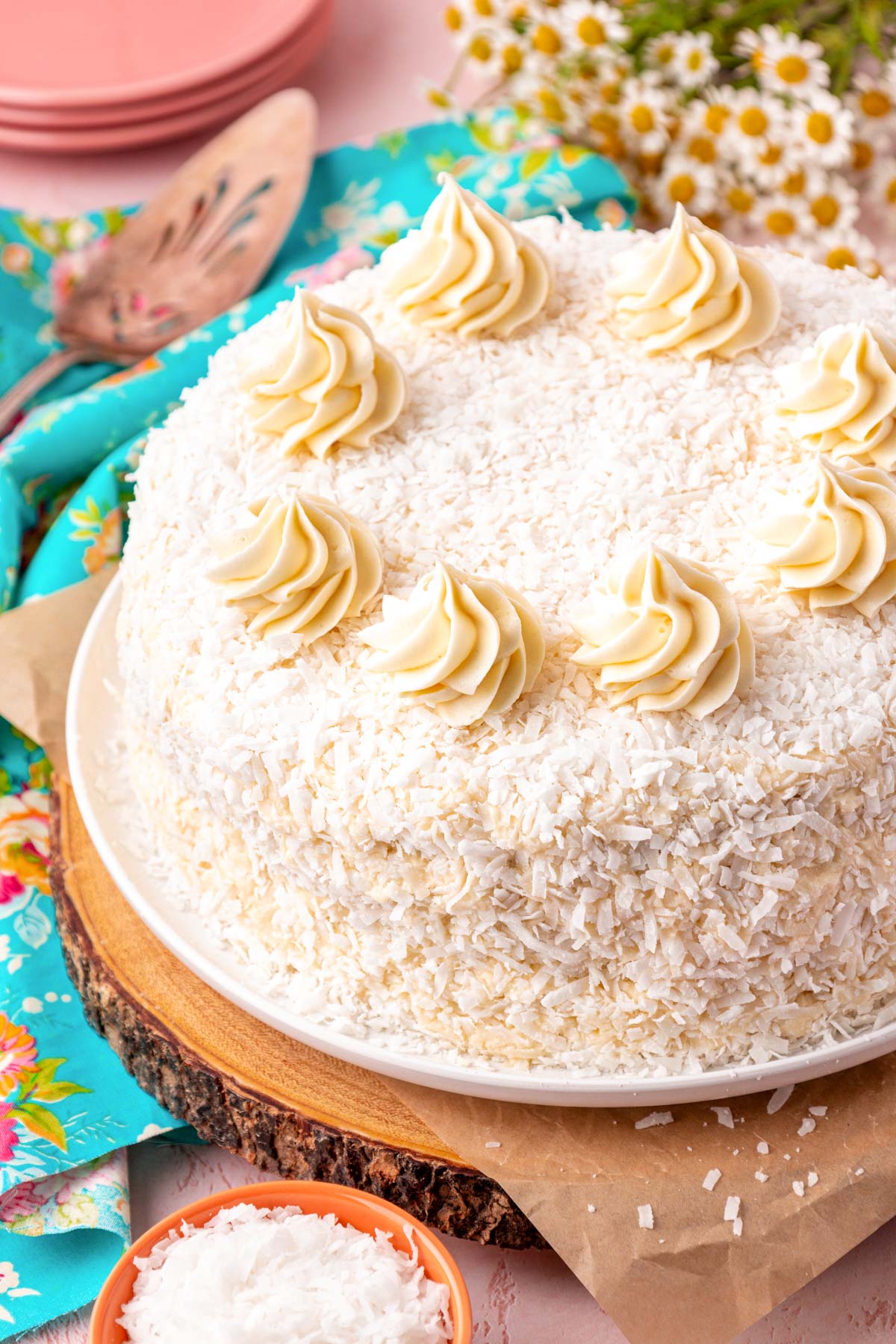 A coconut cake on a wooden cake plate on a table.