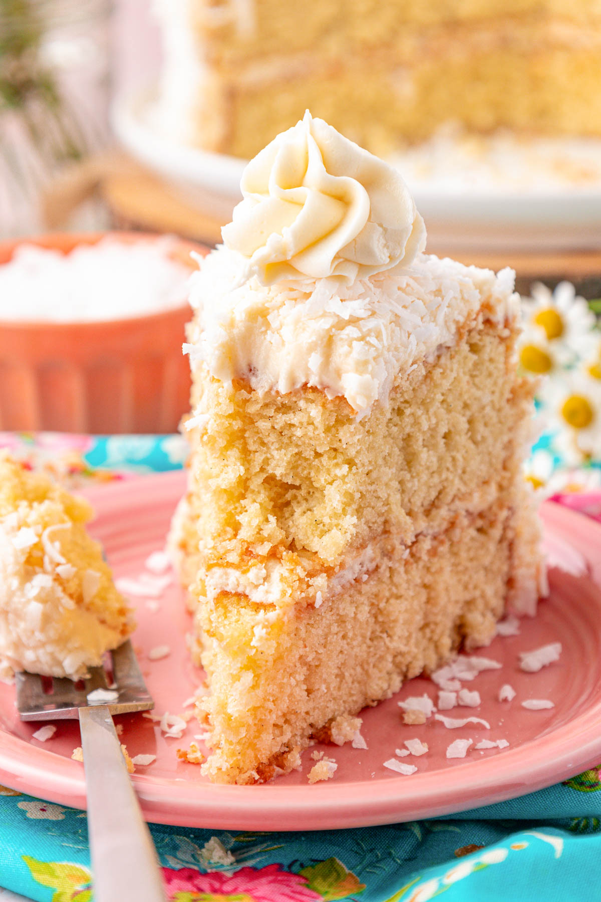 A slice of coconut cake on a pink plate with a bite missing.