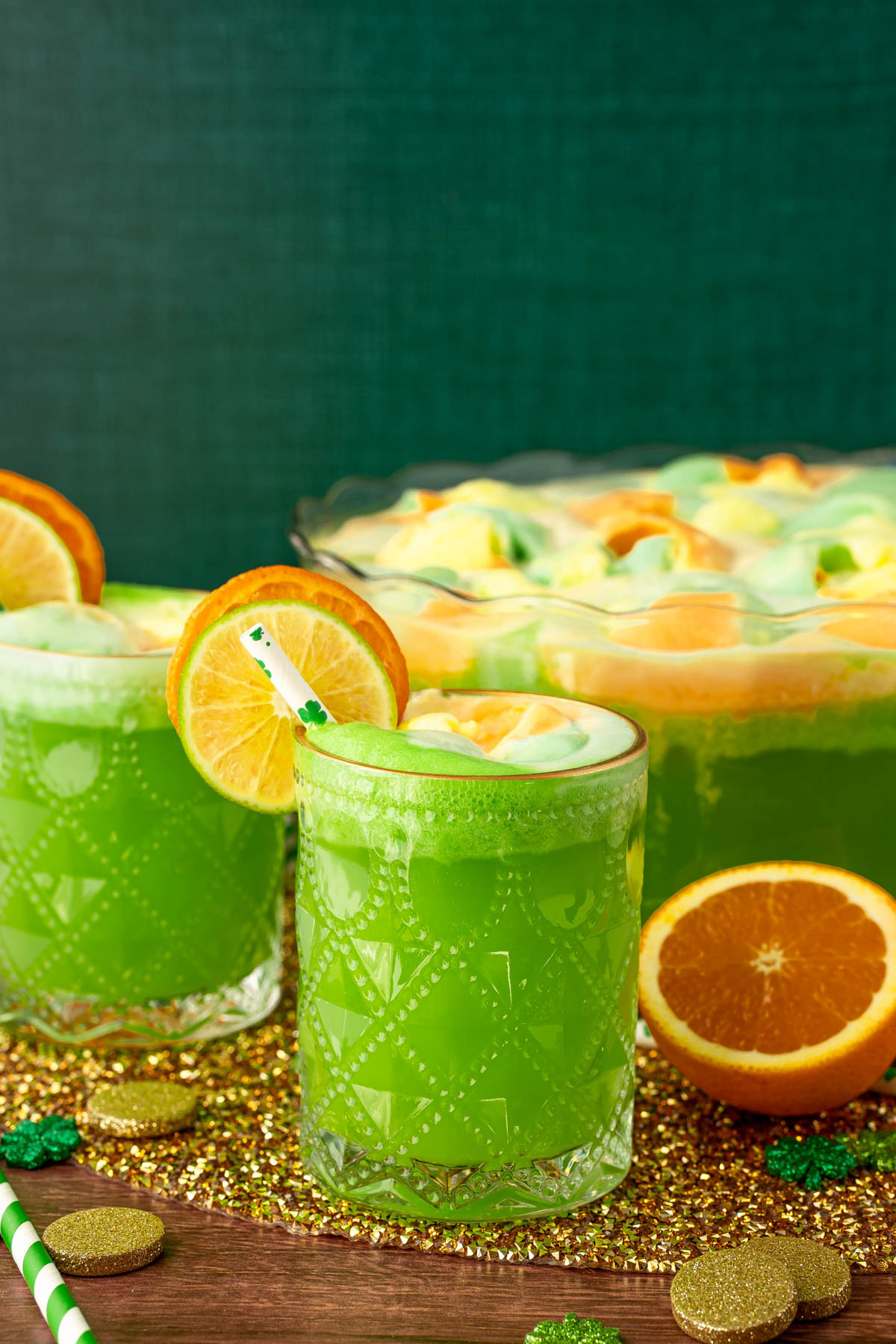 Two glass of green punch in front of a punch bowl at a St. Patrick's day party.