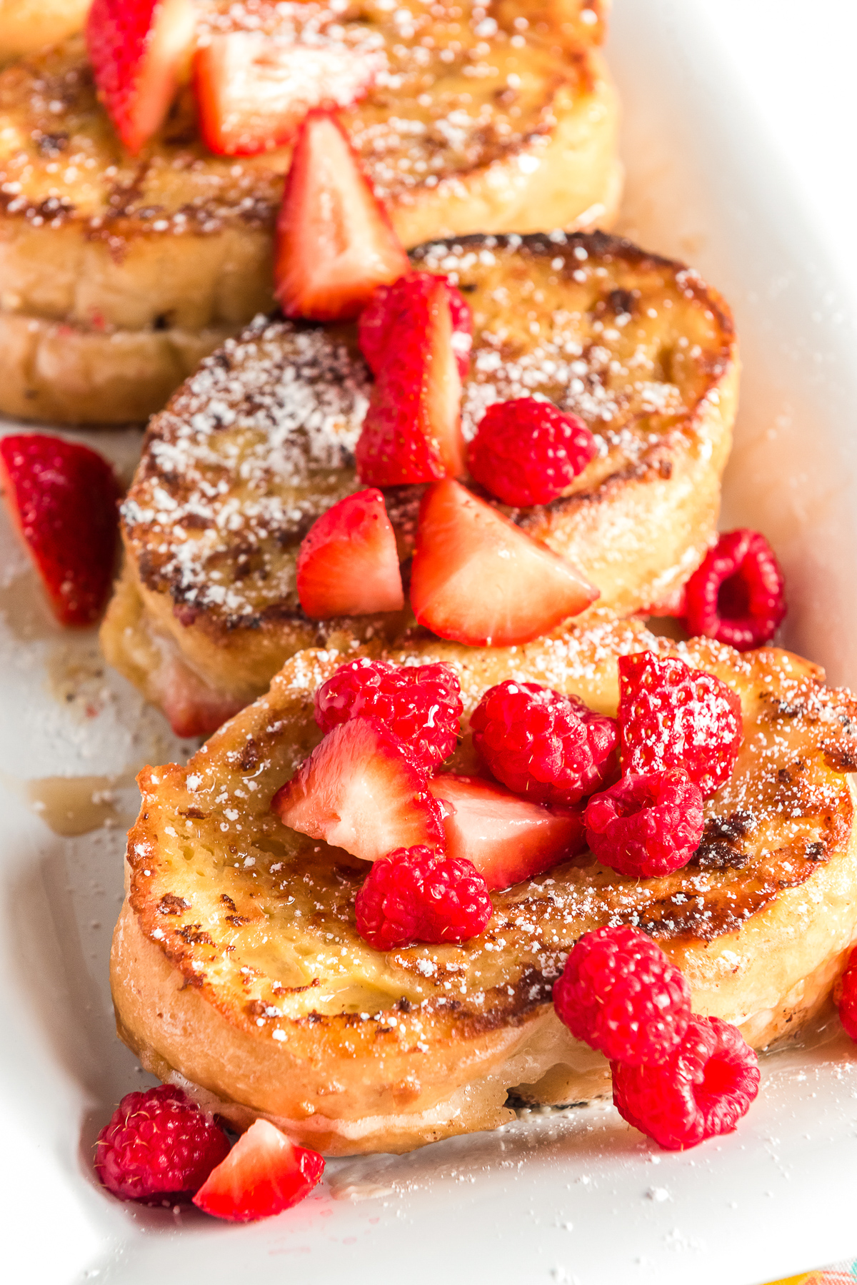 Slices of french toast on a white plate topped with raspberries and strawberries.