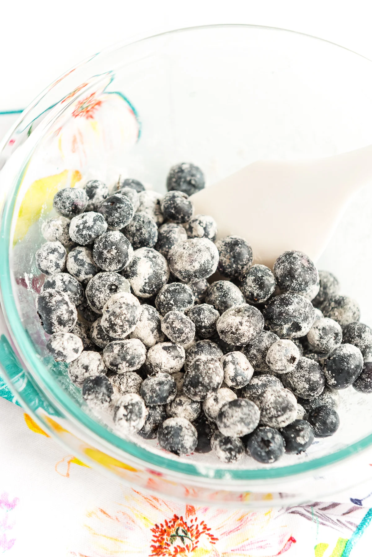 Blueberries being tossed with flour in a large glass bowl.
