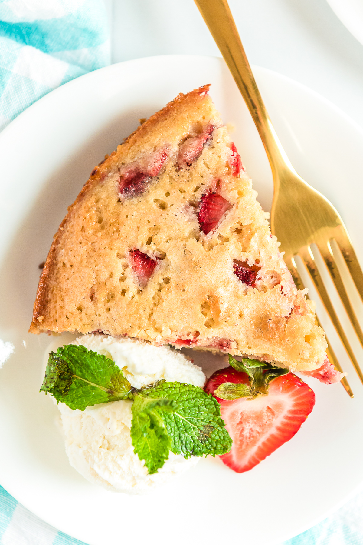 Overhead photo of a slice of strawberry cake on a white plate with whipped cream and gold fork.