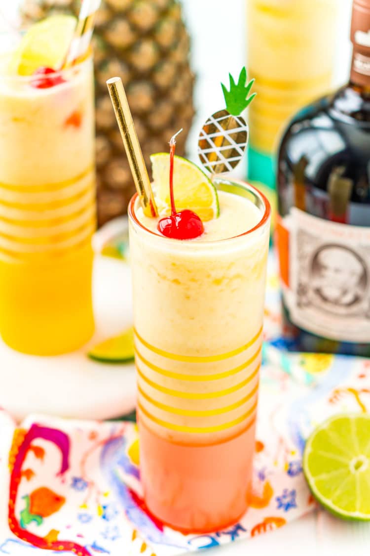 Two glasses filled with a frozen cocktail with a bottle of rum and a pineapple in the background.