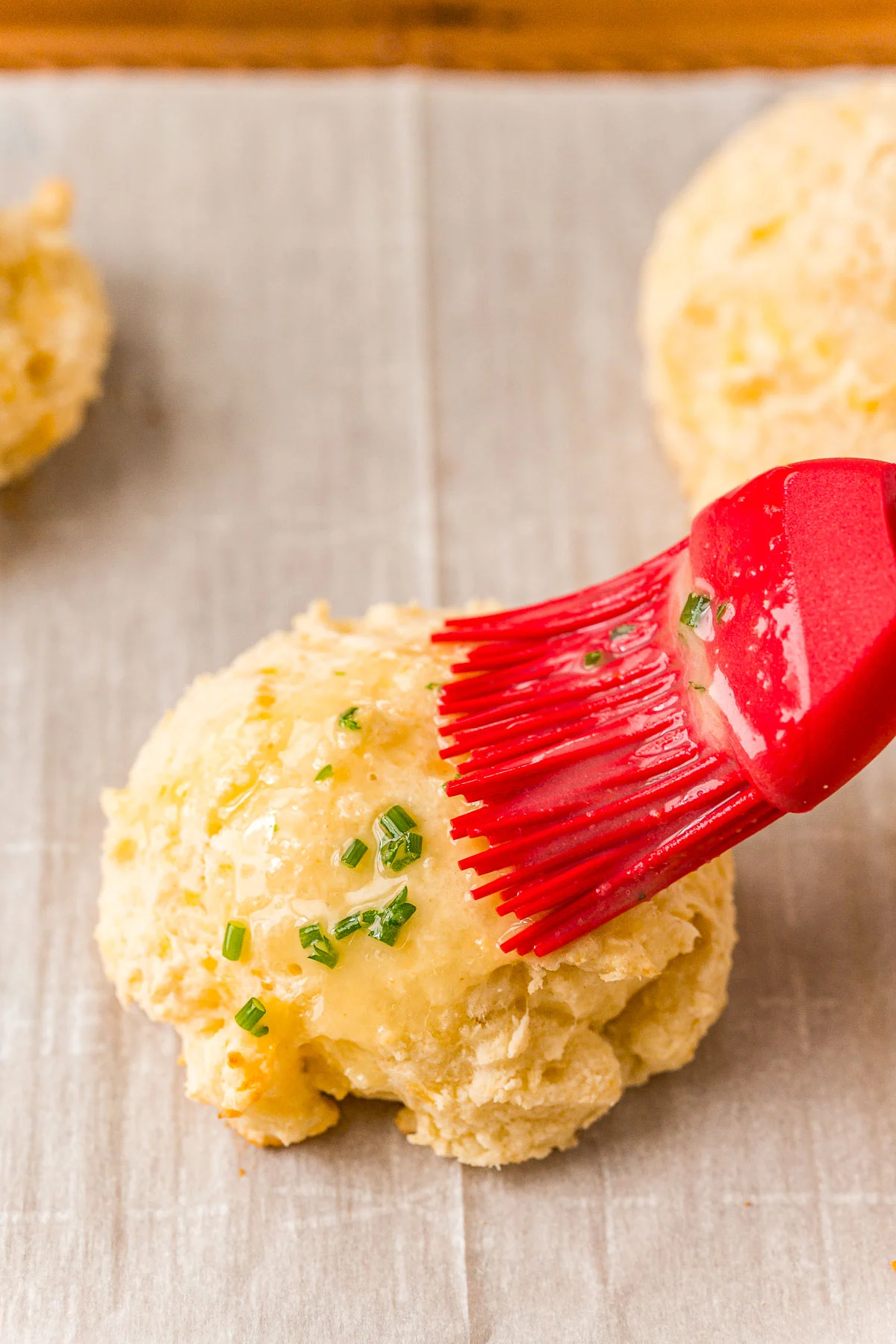 A pastry brush brushing butter on a biscuit.