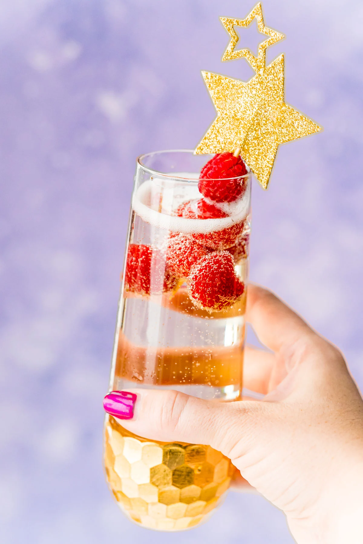 Woman's hand holding up a champagne cocktail with raspberry garnish.
