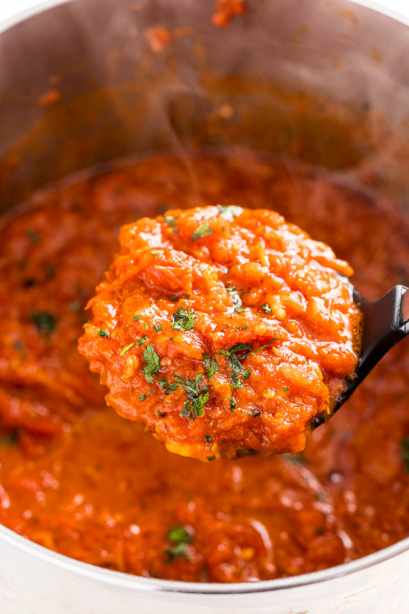 A ladle lifting a scoop of homemade marinara sauce out of a pot.