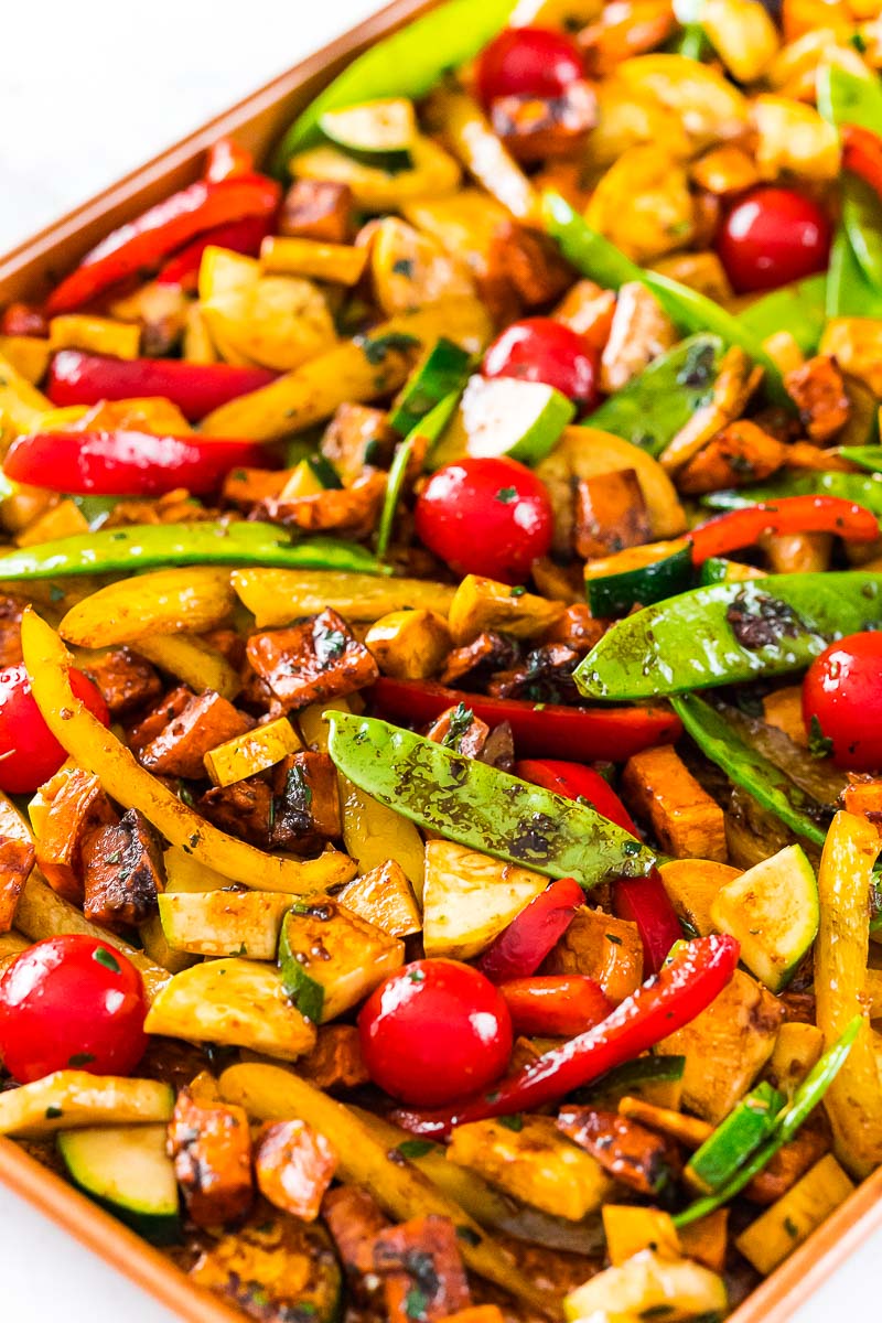 Fresh vegetables coated in dressing on a sheet pan ready to be roasted.
