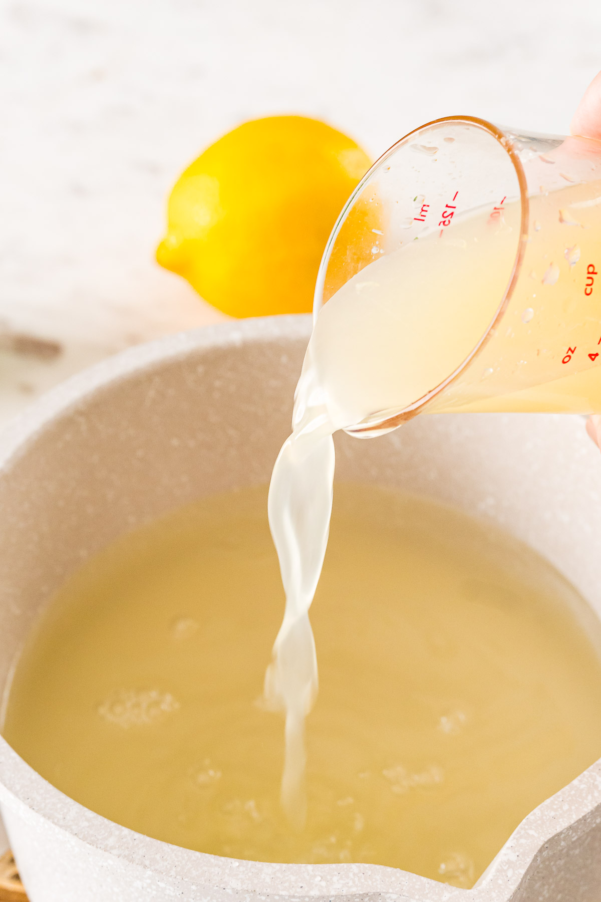 Lemon juice being added to a small pot with water, sugar, and lime juice to make homemade sour mix.
