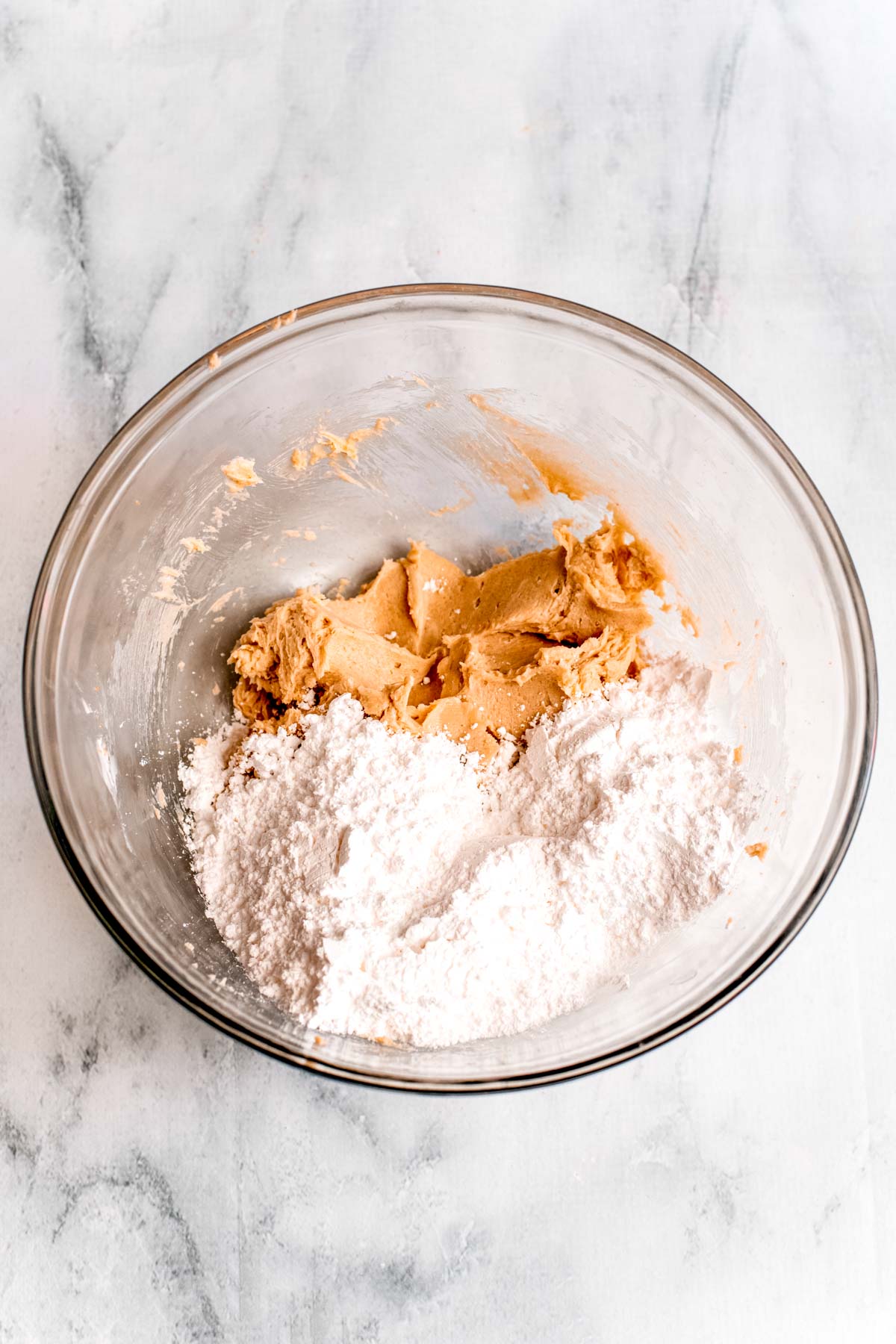 Overhead photo of frosting being made in a glass mixing bowl where powdered sugar has just been added.