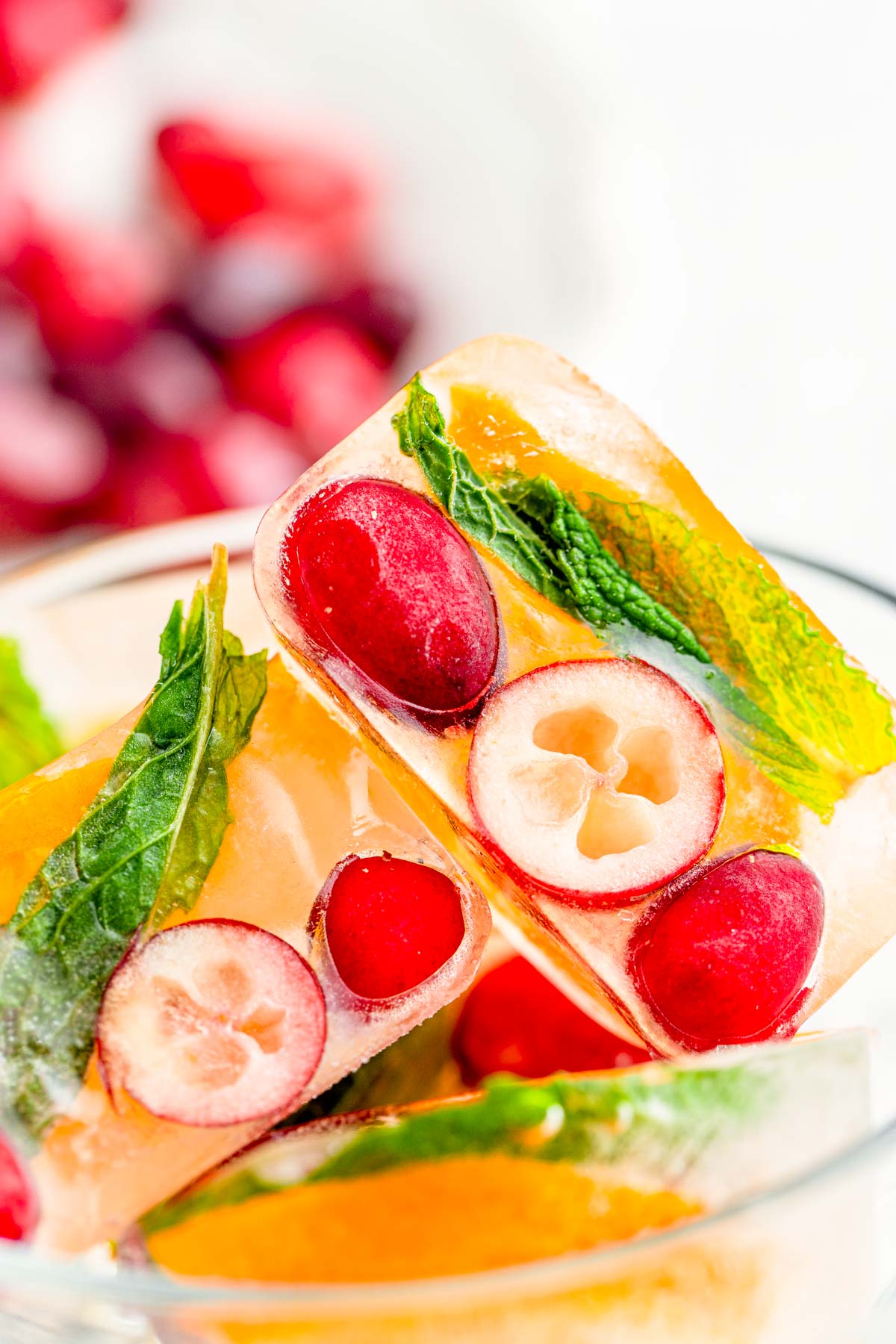 Close up photo of ice cubes with cranberries, orange, and mint in them