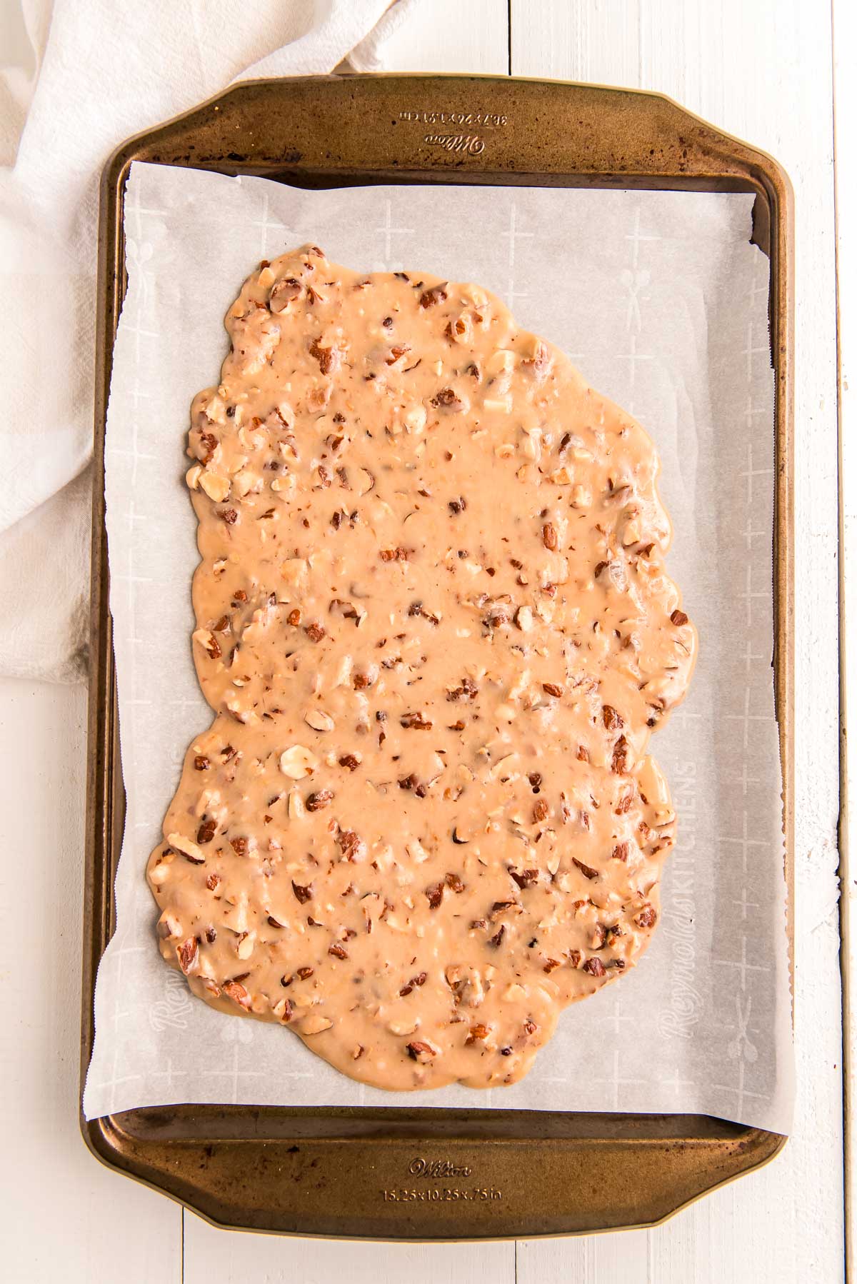 Overhead photo of a baking sheet with toffe spread out on parchment paper.
