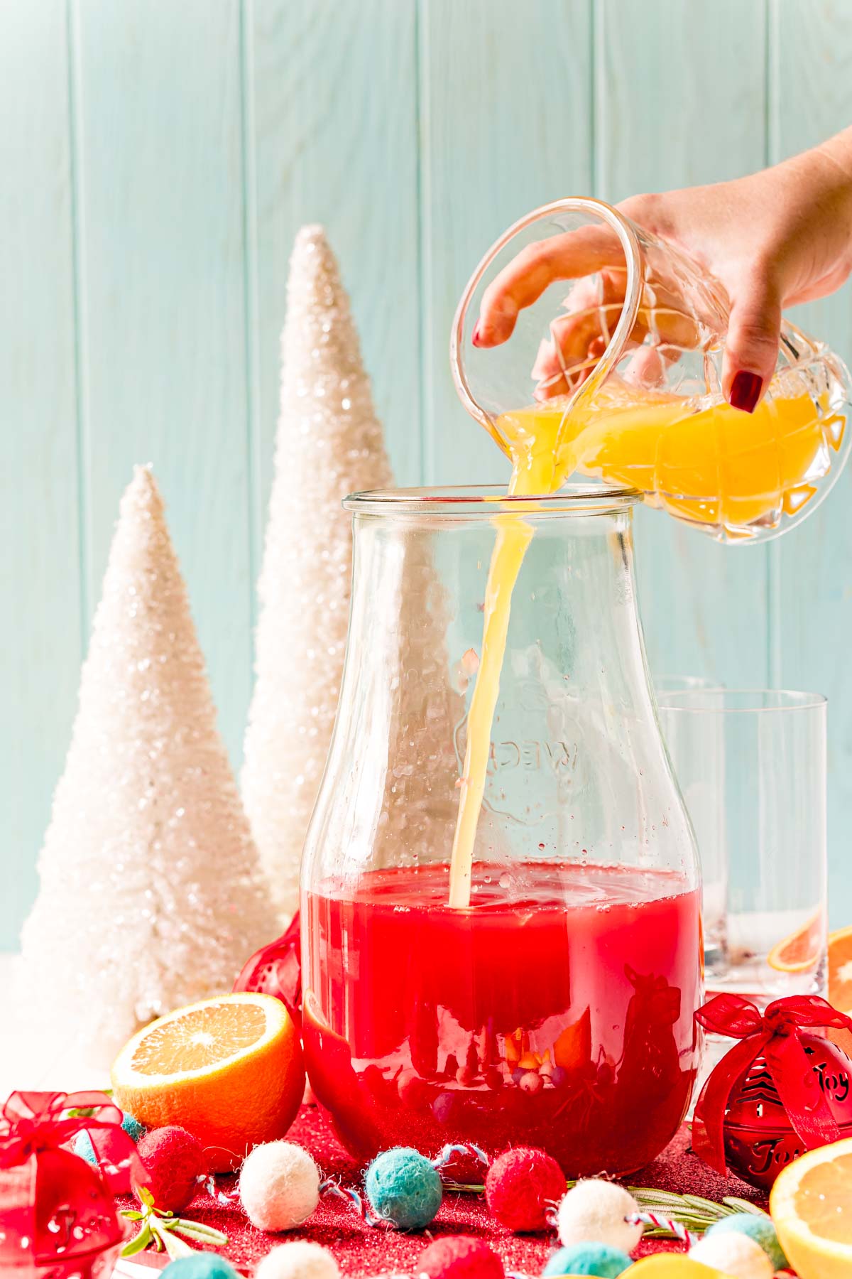 Orange juice being poured into a pitcher with other juices.