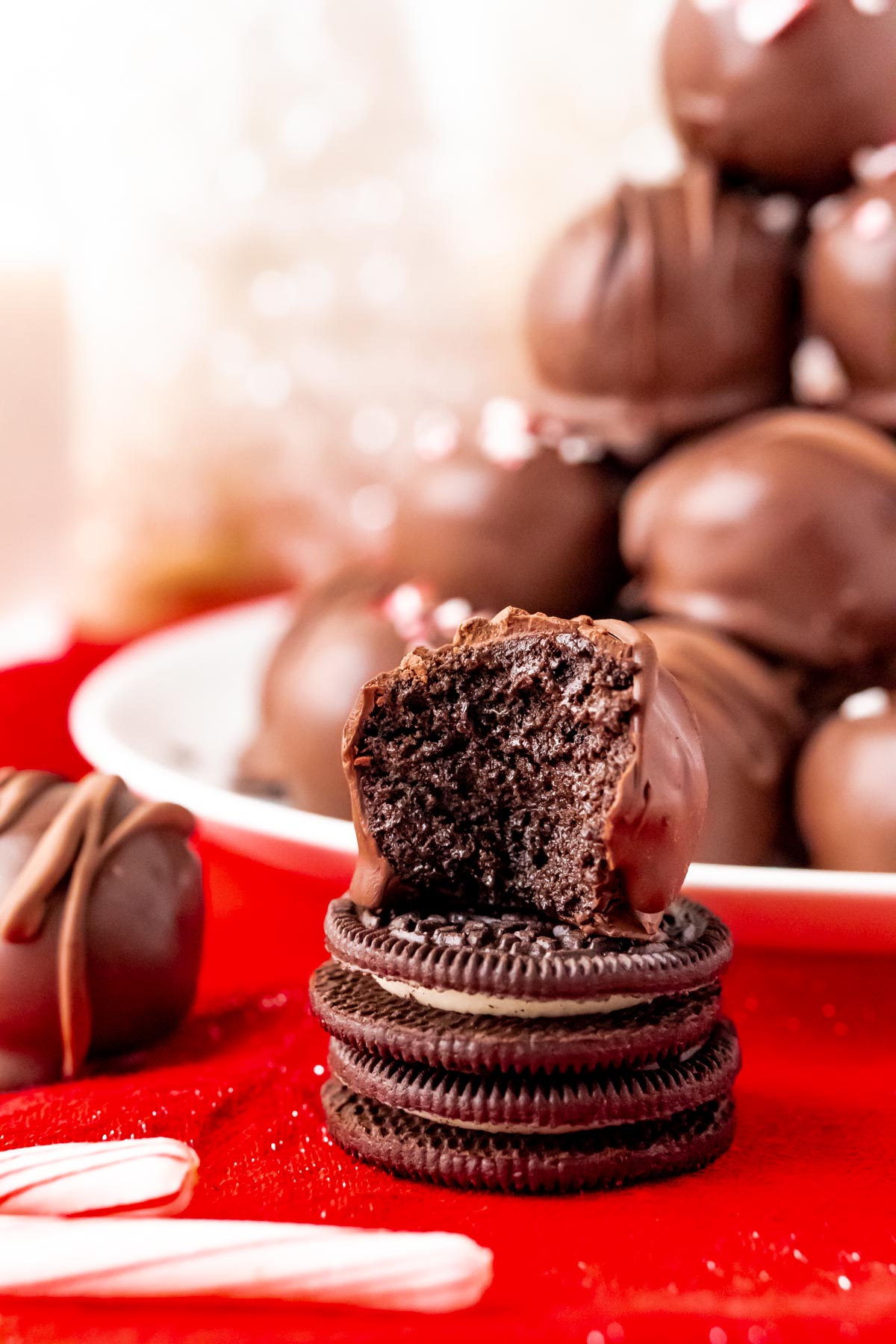 Close up photo of an oreo ball on a stack of 2 oreos in front of a plate of balls.