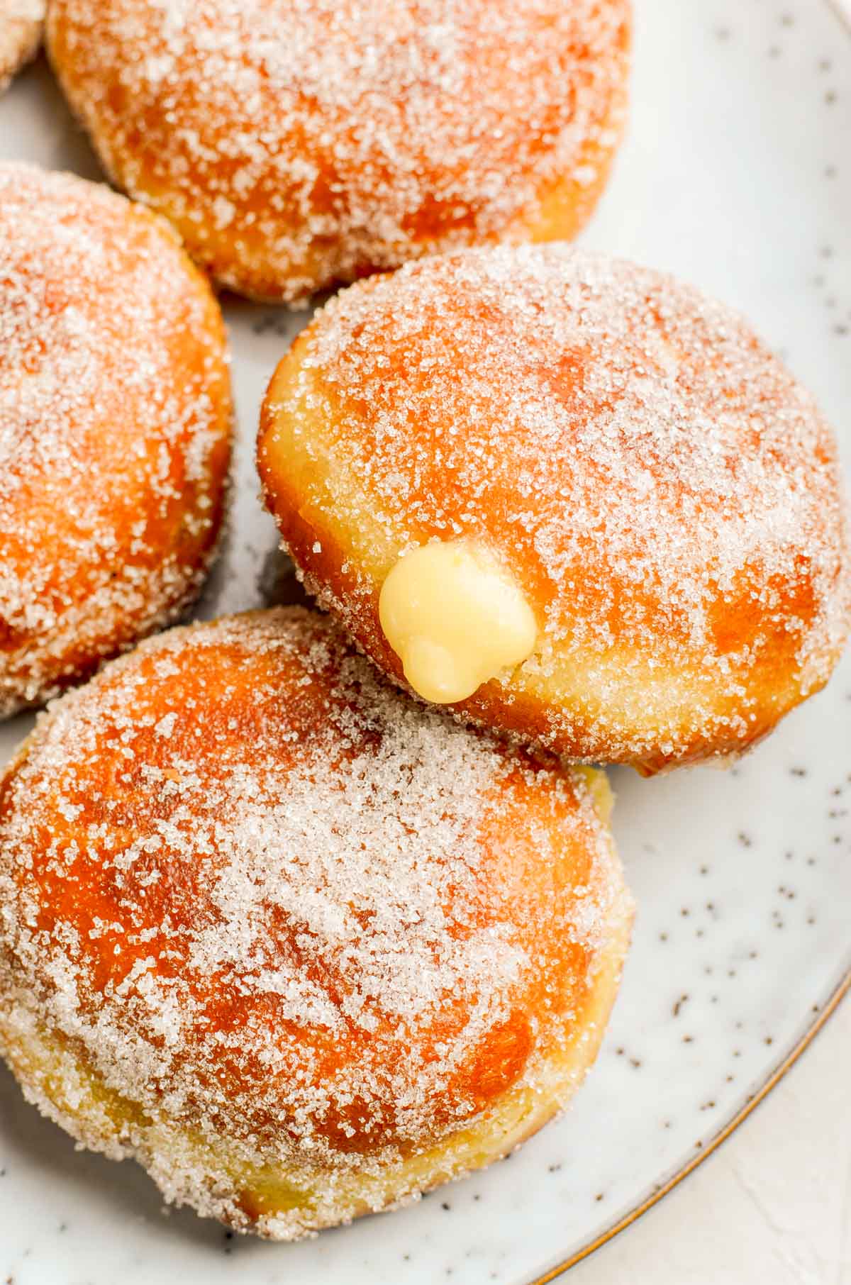 Close up photo of sugared donuts filled with pastry cream on a plate.