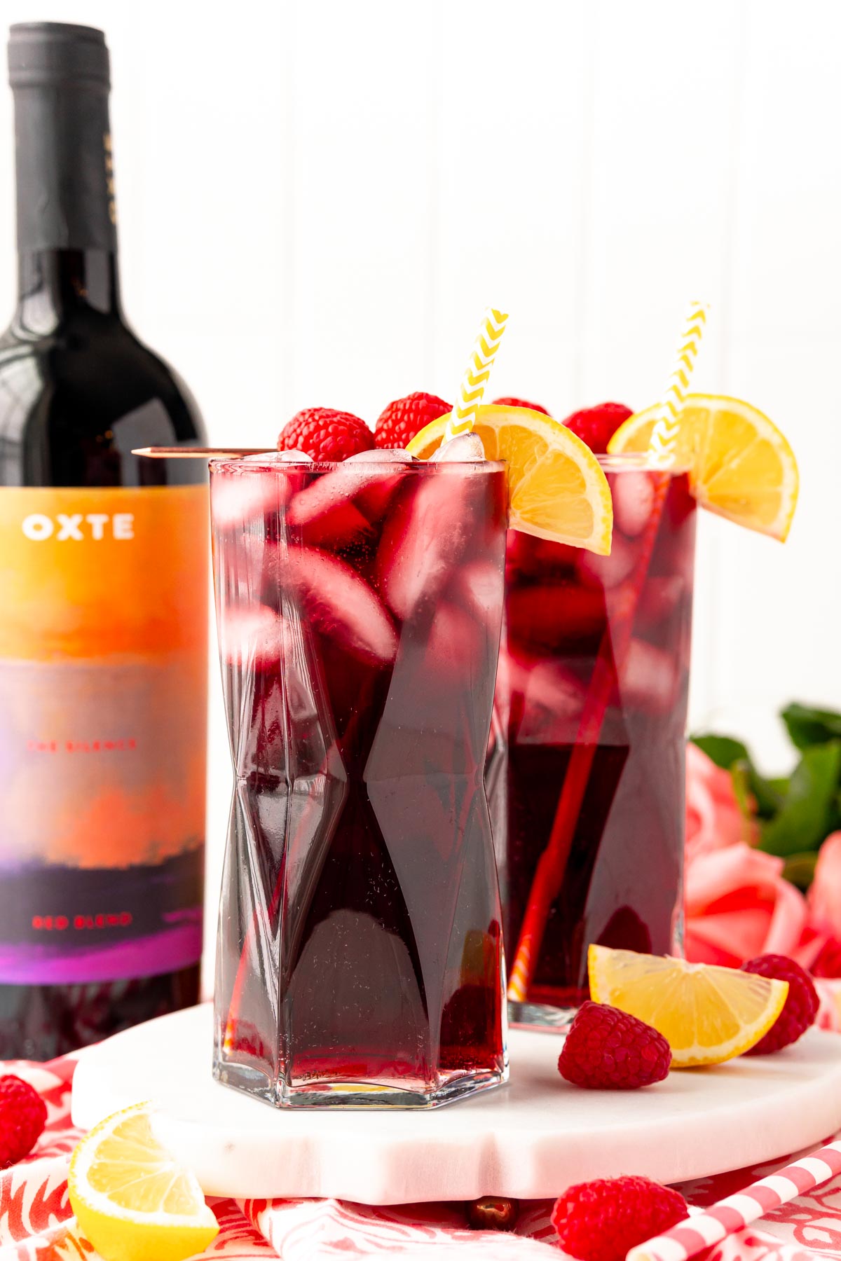 Straight on photo of two glasses filled with red wine spritzers on a marble tray with a bottle of red wine in the background.