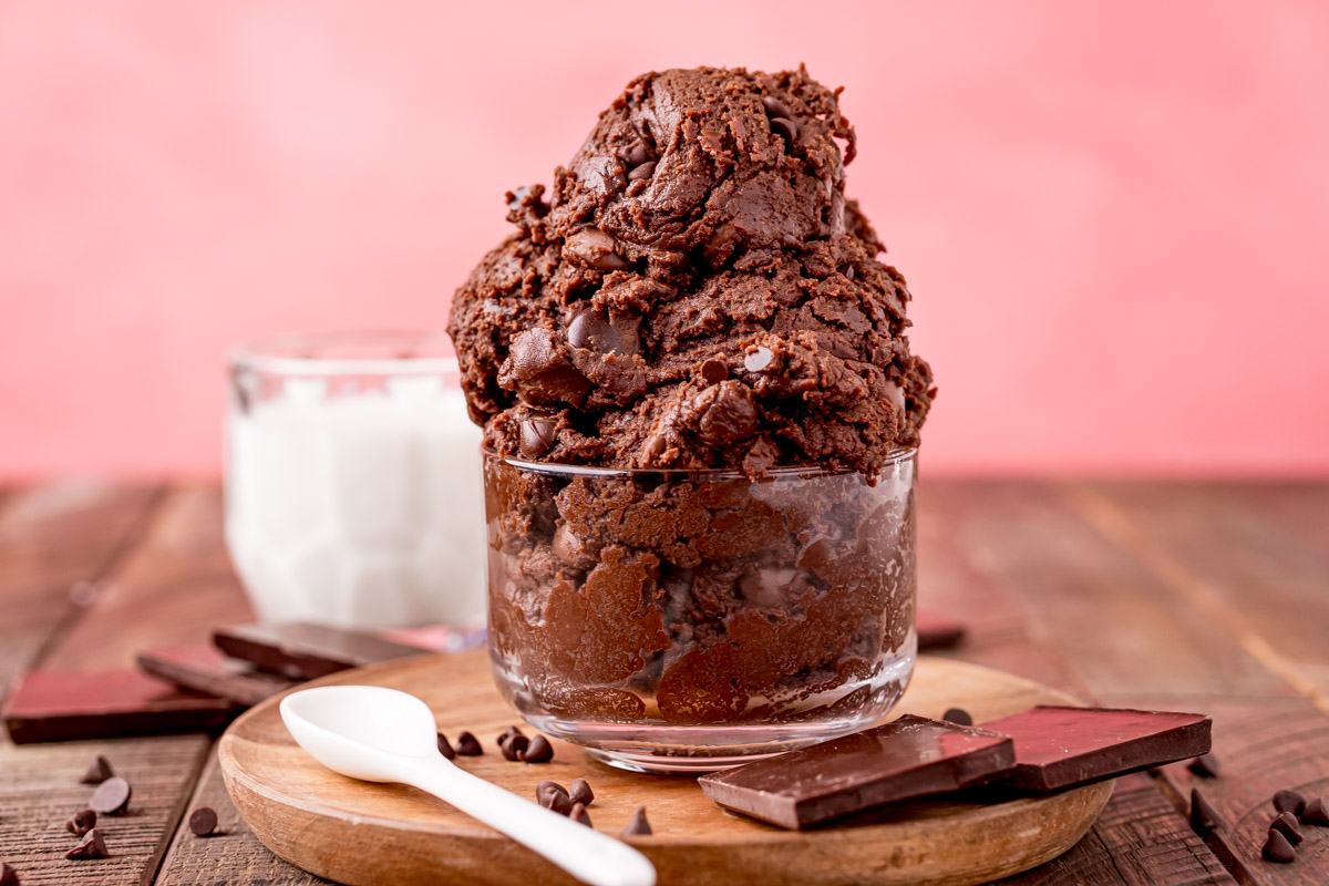 Close up photo of edible brownie batter in a glass bowl with milk behind it.