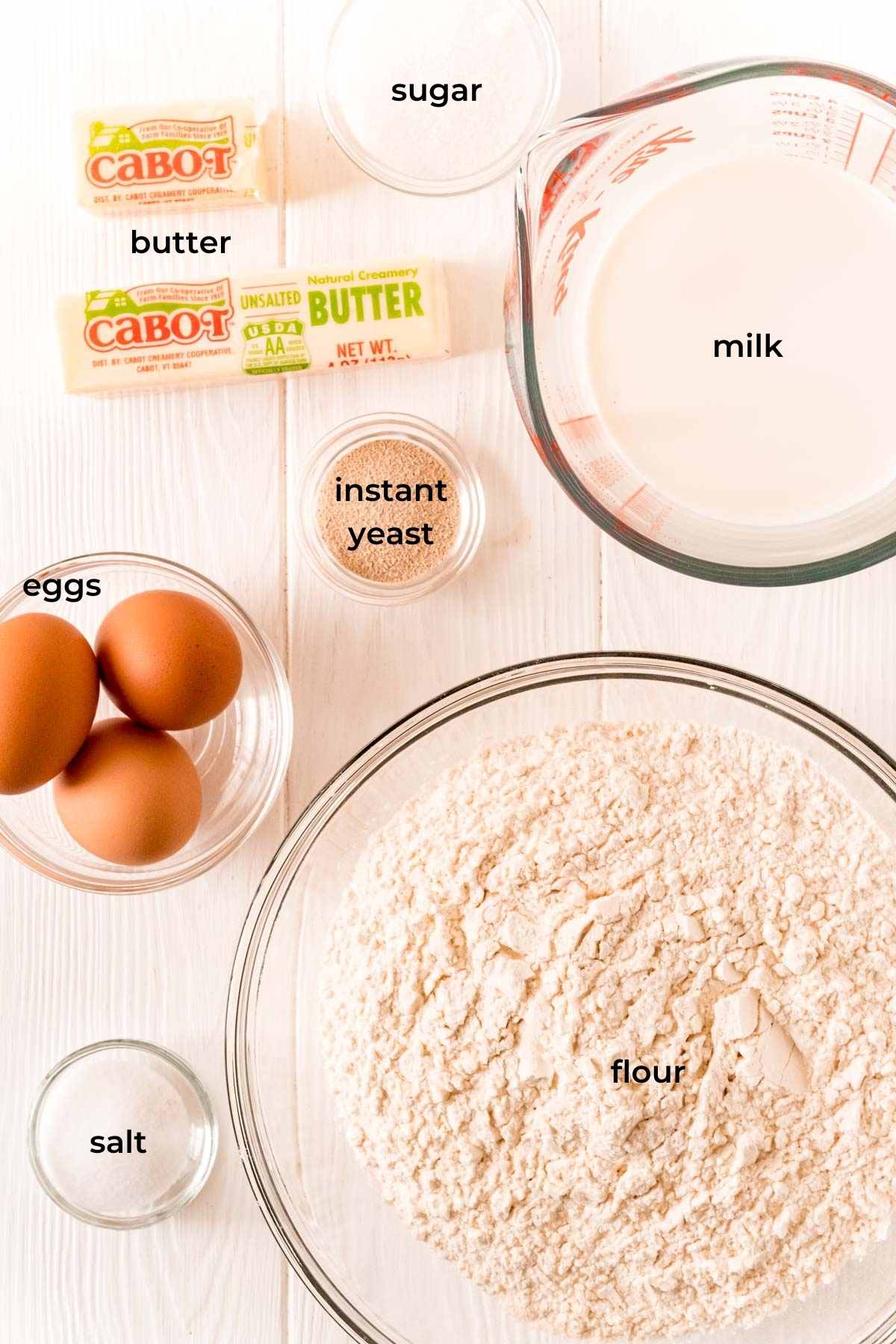 Ingredients to make parker house dinner rolls on a white wood table.