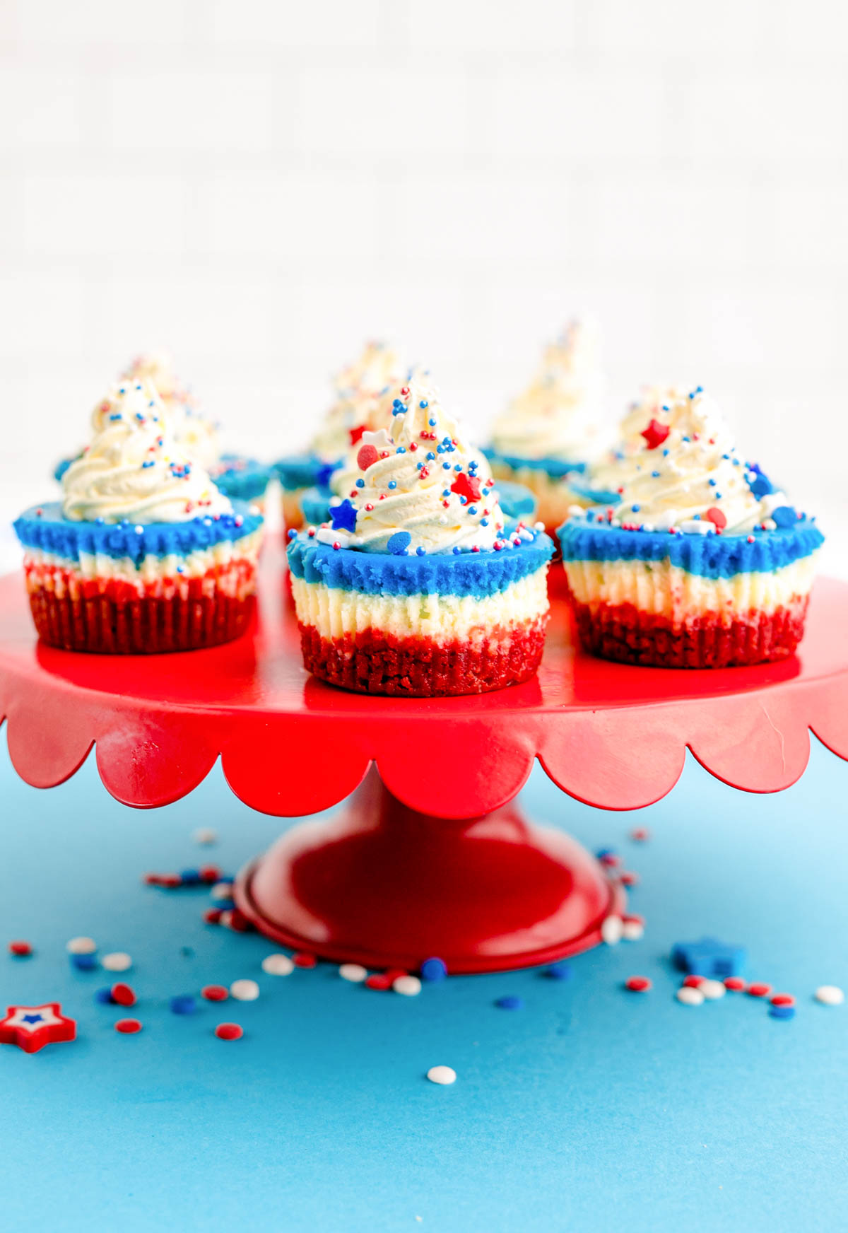 red, white, and blue mini cheesecakes for the 4th of july on a red cake stand on a blue surface.